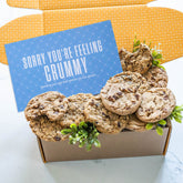 Open gift box filled with assorted cookies and greenery, with a blue card that reads âSorry Youâre Feeling Crummy.â
