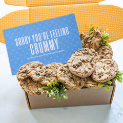 Open gift box filled with assorted cookies and greenery, with a blue card that reads âSorry Youâre Feeling Crummy.â