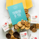 Open yellow gift box with assorted cookies, greenery, and a blue card that reads âThinking of You.â