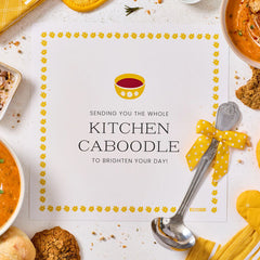 Card with a decorative border that reads âSending You the Whole Kitchen Caboodle to Brighten Your Day,â surrounded by soup, cookies, and a metal ladle with a yellow ribbon.