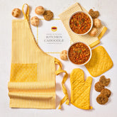 Overhead view of a kitchen-themed arrangement with two bowls of soup, rolls, cookies, a striped apron, matching oven mitts, and a card that reads âKitchen Caboodle.â
