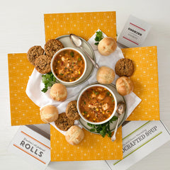 Top-down view of soup, bread rolls, and cookies arranged on a yellow box.