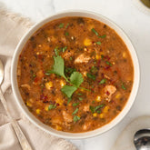 Close-up of a bowl of hearty soup with chicken, corn, herbs, and spices, garnished with fresh cilantro.