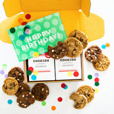 Open yellow gift box filled with assorted cookies and two boxes labeled âCookies Goodness,â with a green card that reads âHappy Birthdayâ and colorful confetti scattered around.