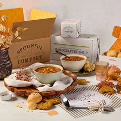 Overhead view of a fall-themed arrangement with two bowls of soup, rolls, cookies, a box labeled âHandcrafted Soup,â a box of rolls, a metal ladle with a yellow ribbon, autumn leaves, and a card that reads âFeels Like Fall.â