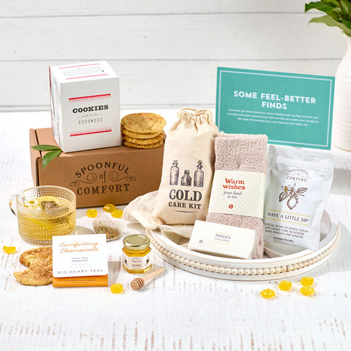 Self-care gift set arranged on a tray with tea, cookies, a candle, bath and body products, a jar of honey, and a card that reads âSome Feel Better Finds.â