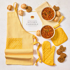 Overhead view of a kitchen-themed arrangement with two bowls of soup, rolls, cookies, a striped apron, matching oven mitts, and a card that reads âKitchen Caboodle.â