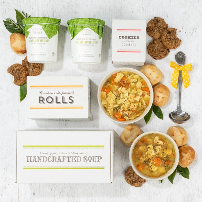 Overhead view of a soup gift arrangement with two bowls of chicken soup, rolls, cookies, two containers of soup with green lids, a box labeled âHandcrafted Soup,â a box of rolls, a box of cookies, and a metal ladle with a yellow ribbon.