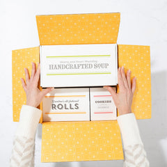 Open yellow gift box displaying a card that reads âLove by the Spoonfulâ and a metal ladle with a yellow ribbon inside.