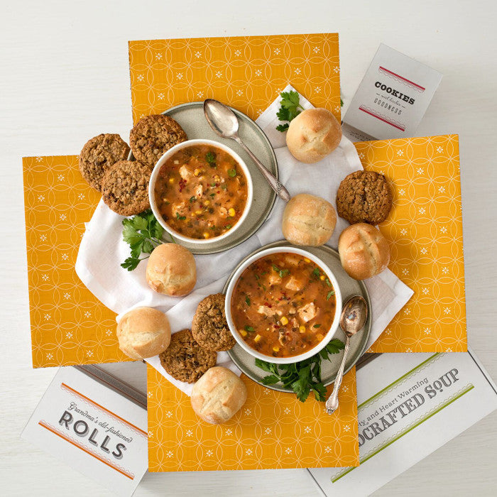 Top-down view of soup, bread rolls, and cookies arranged on a yellow box.