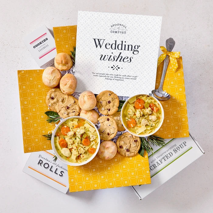 Overhead view of a yellow gift box arrangement with two bowls of soup, rolls, cookies, a container labeled âHandcrafted Soup,â a metal ladle with a yellow ribbon, and a card that reads âWedding Wishes.â