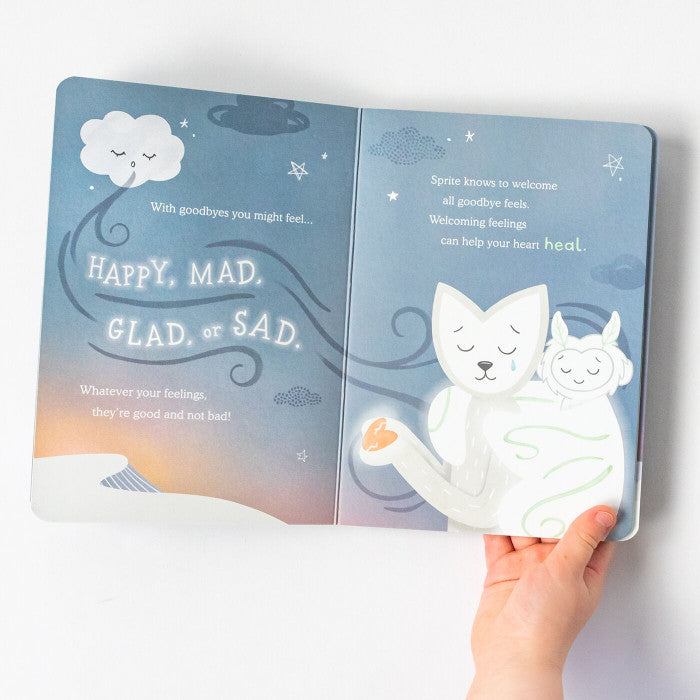Hand holding an open childrenâs book with illustrated animal characters and text about emotions, including âHappy, Mad, Glad, Sad,â on softly colored pages.
