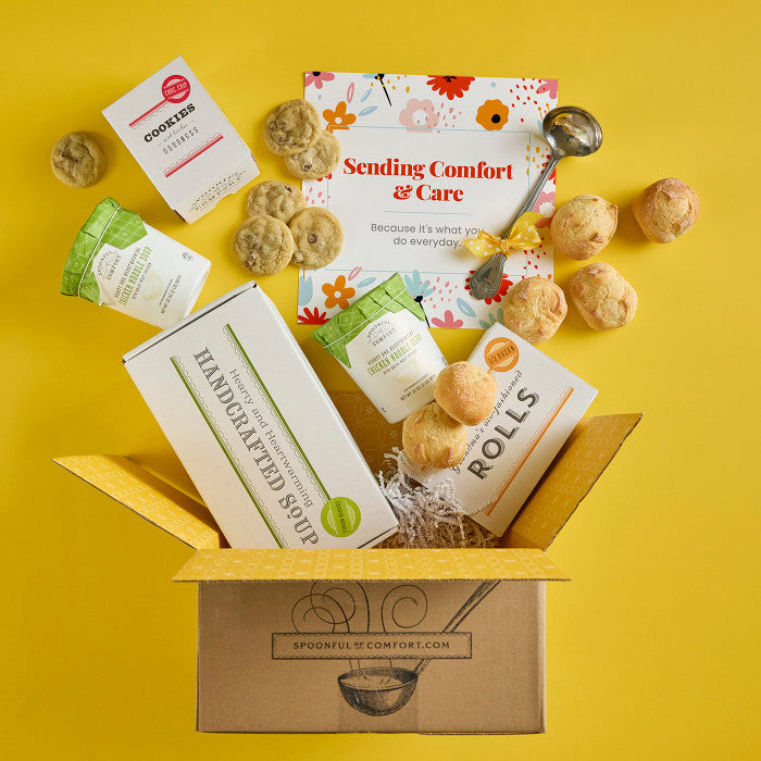 Open Spoonful of Comfort gift box with rolls, cookies, two containers of soup, a box labeled âHandcrafted Soup,â and a floral card that reads âSending Comfort & Care,â with additional rolls and cookies arranged around the box.