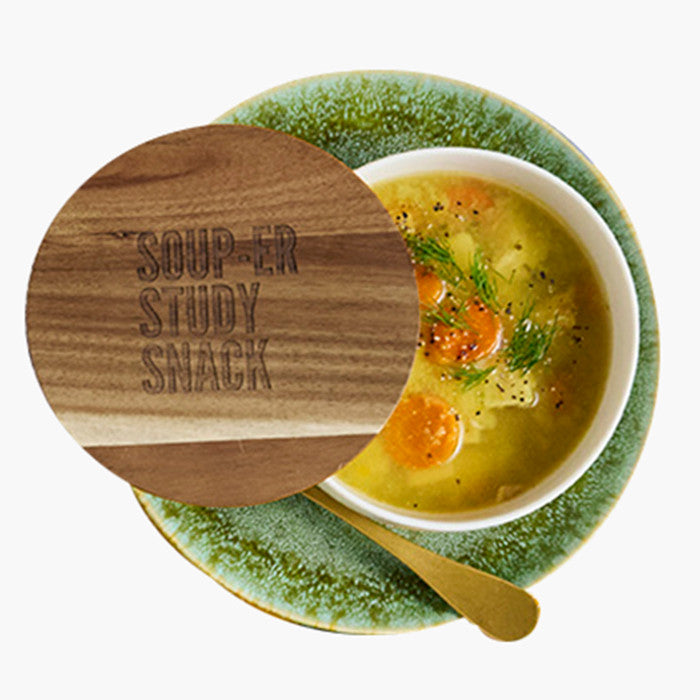 Close-up of a bowl of soup on a green plate with a wooden lid engraved âSoup-er Study Snack,â partially covering the bowl.