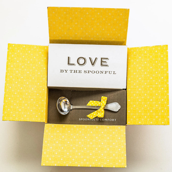 Open yellow gift box displaying a card that reads âLove by the Spoonfulâ and a metal ladle with a yellow ribbon inside.