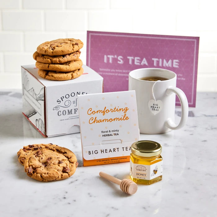 Tea-themed gift arrangement with cookies, a mug, chamomile tea, a jar of honey with a wooden dipper, and a card that reads âItâs Tea Time.â