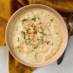 Close-up of a bowl of loaded baked potato soup topped with herbs and seasoning, set beside a spoon and a yellow cloth.