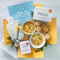 Pregnancy Care Package with soup, rolls, cookies, a fuzzy old fashioned heat pack, and a insert with text "Bun in your oven, soup in your bowl"