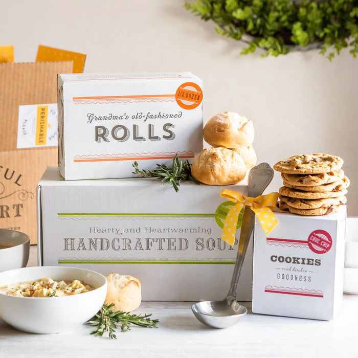 Soup gift set displayed with a bowl of soup, rolls, cookies, boxes labeled âChicken Soup,â âRolls,â and âCookies,â and a metal ladle with a yellow ribbon.