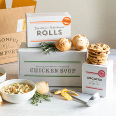 Soup gift set displayed with a bowl of chicken soup, rolls, cookies, boxes labeled âChicken Soup,â âRolls,â and âCookies,â and a metal ladle with a yellow ribbon.