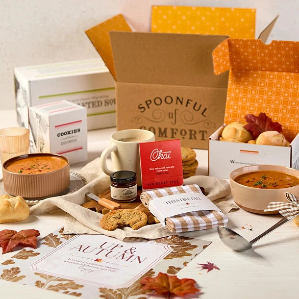 Overhead view of a fall-themed gift arrangement with two bowls of soup, rolls, a container labeled âHandcrafted Soup,â a metal ladle with a yellow ribbon, autumn leaves, and a card that reads âUp and Autumn.â