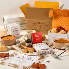 Overhead view of a fall-themed gift arrangement with two bowls of soup, rolls, a container labeled âHandcrafted Soup,â a metal ladle with a yellow ribbon, autumn leaves, and a card that reads âUp and Autumn.â