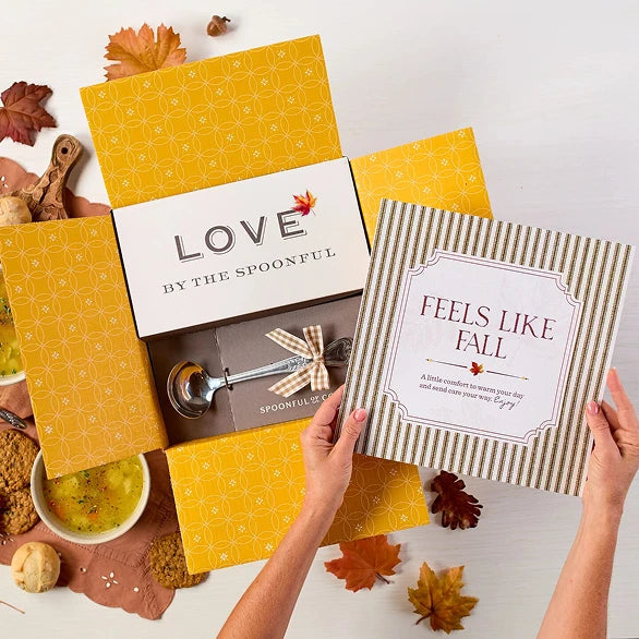 Overhead view of a fall-themed arrangement with two bowls of soup, rolls, cookies, a box labeled âHandcrafted Soup,â a box of rolls, a metal ladle with a yellow ribbon, autumn leaves, and a card that reads âFeels Like Fall.â