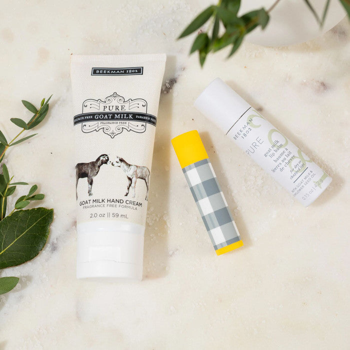 Close-up of self-care items including a tube of milk hand cream, and lip balm arranged with greenery on a light surface.