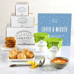 Soup gift set arranged with a bowl of soup, rolls, cookies, two containers of soup with green lids, Spoonful of Comfort boxes, a metal ladle with a yellow ribbon, and a blue card that reads âLoved & Missed.â